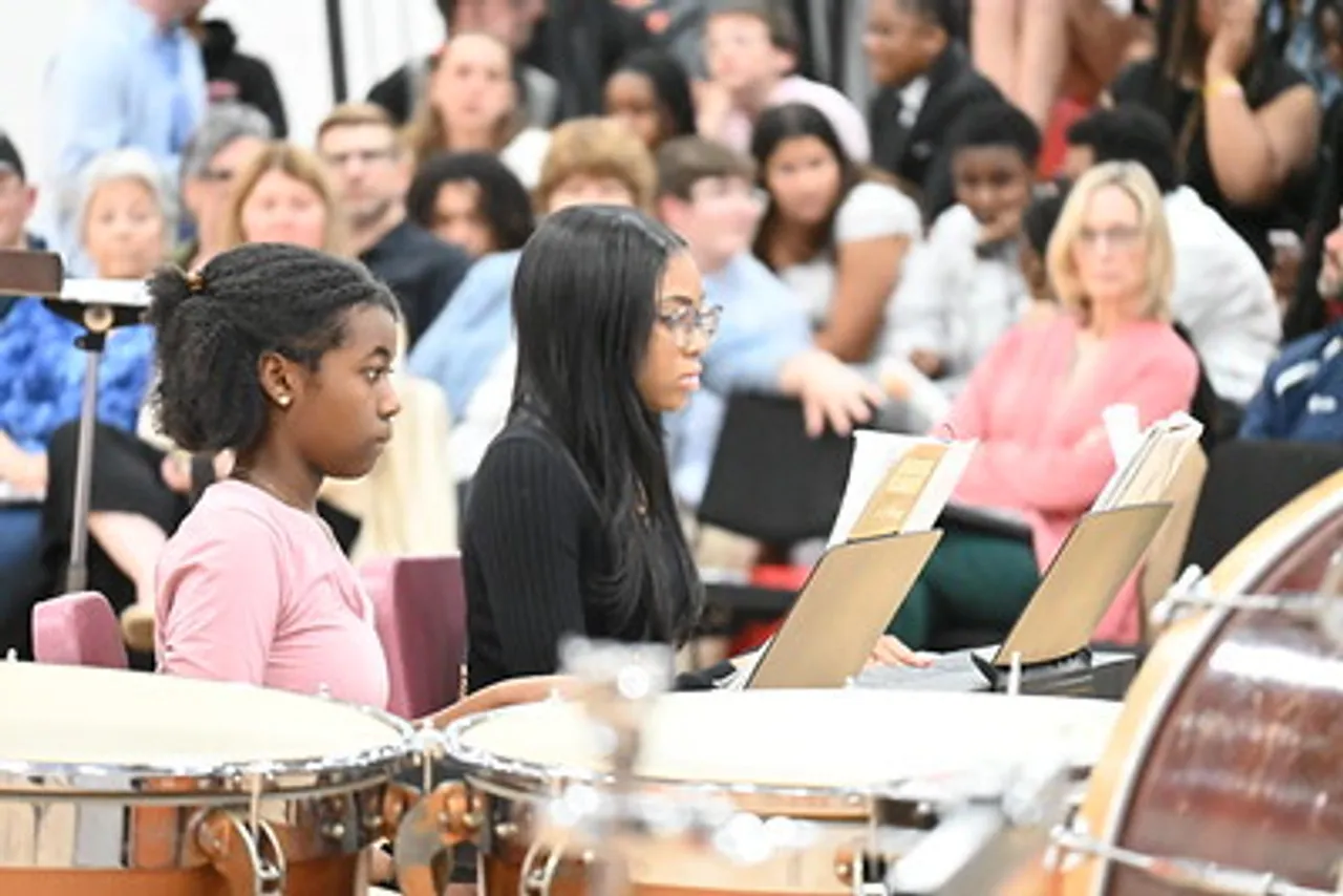 Middle School students playing in the band at a performance with audience behind them.