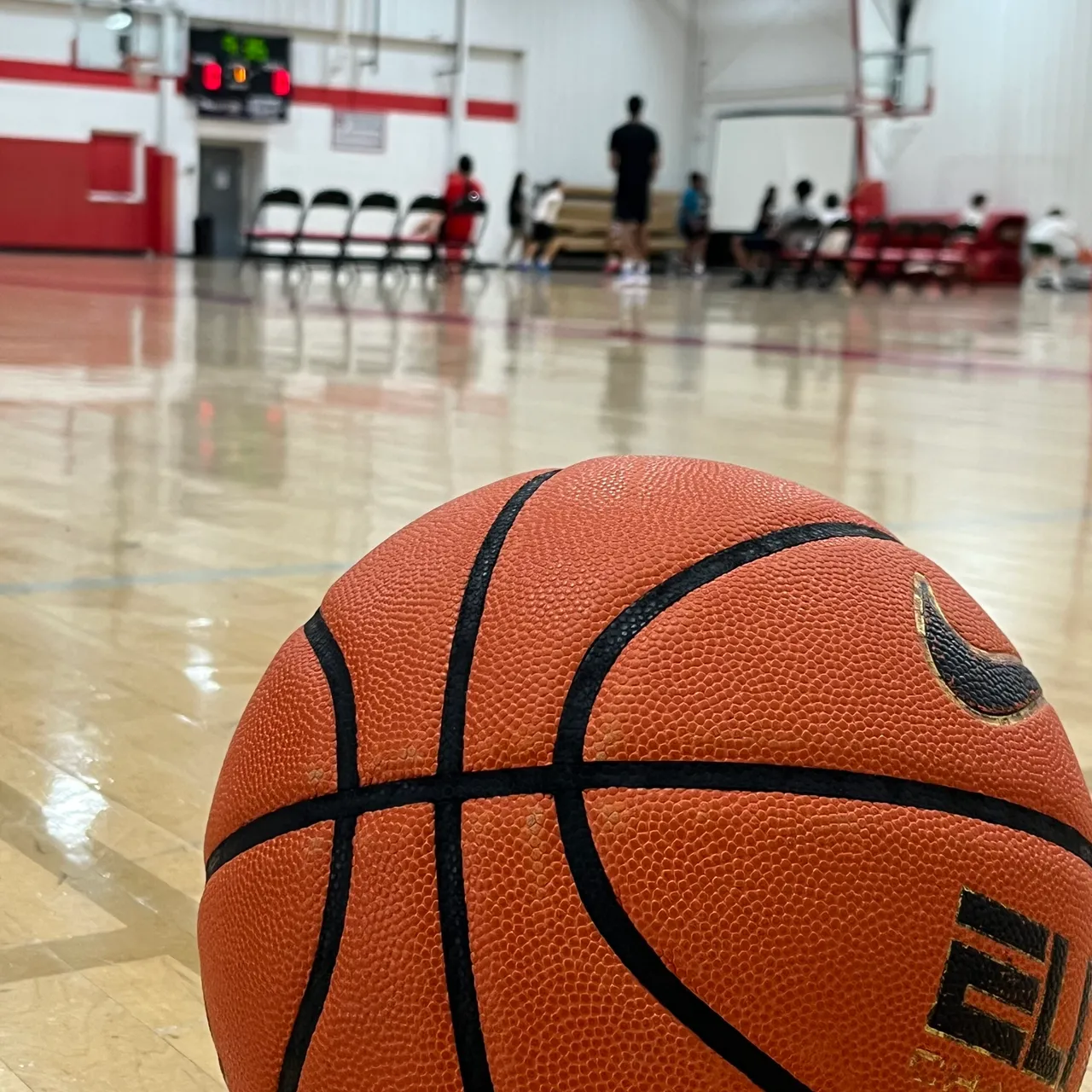 Campers participating in drills in the gym during basketball camp with a basketball in the foreground of the photo.