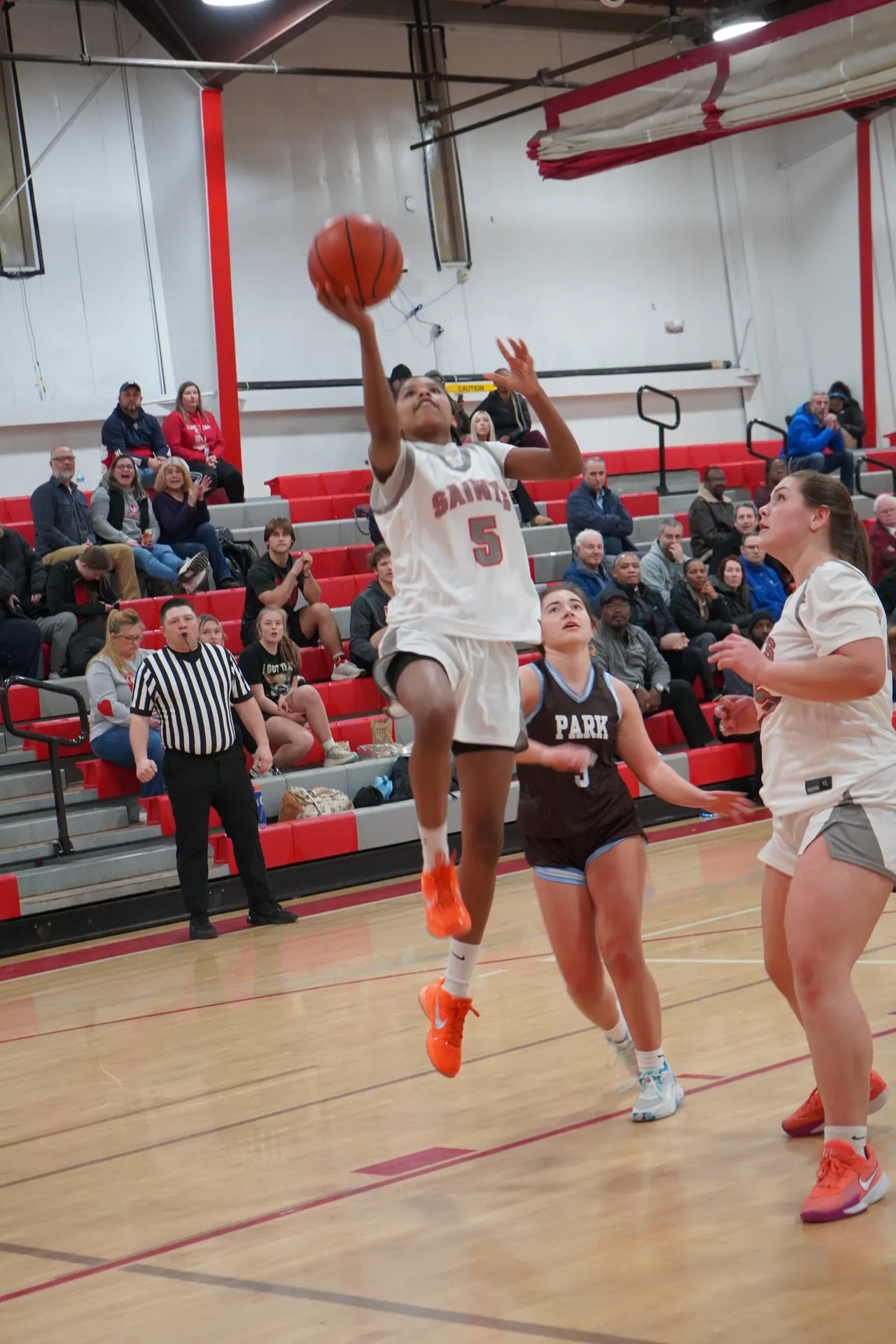 Girls Basketball teammate jumping up to make a shot with two others watching during a game in the gym.