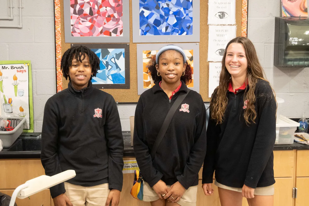 Three students posing in front of their artwork