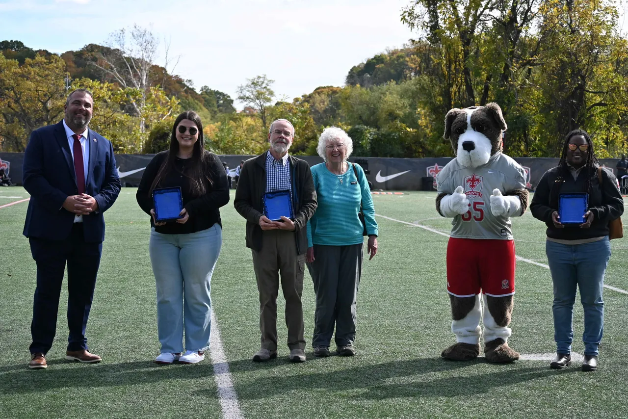 Distinguished Alumni Award recipients and Hall of Fame inductees smile and pose with Headmaster Brent Johnson and Luther the Saint Bernard on Saints Field