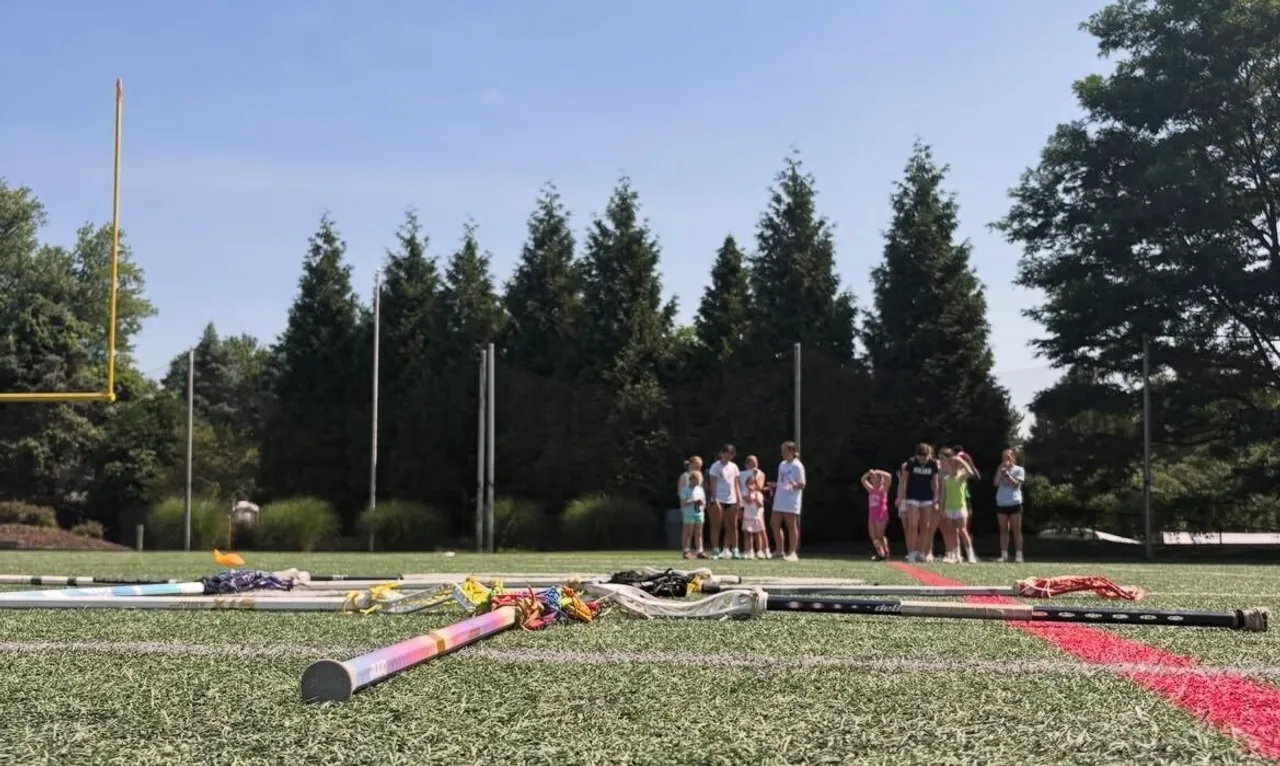 Campers lined up on Saints Field with lacrosse sticks on the ground preparing for a drill.