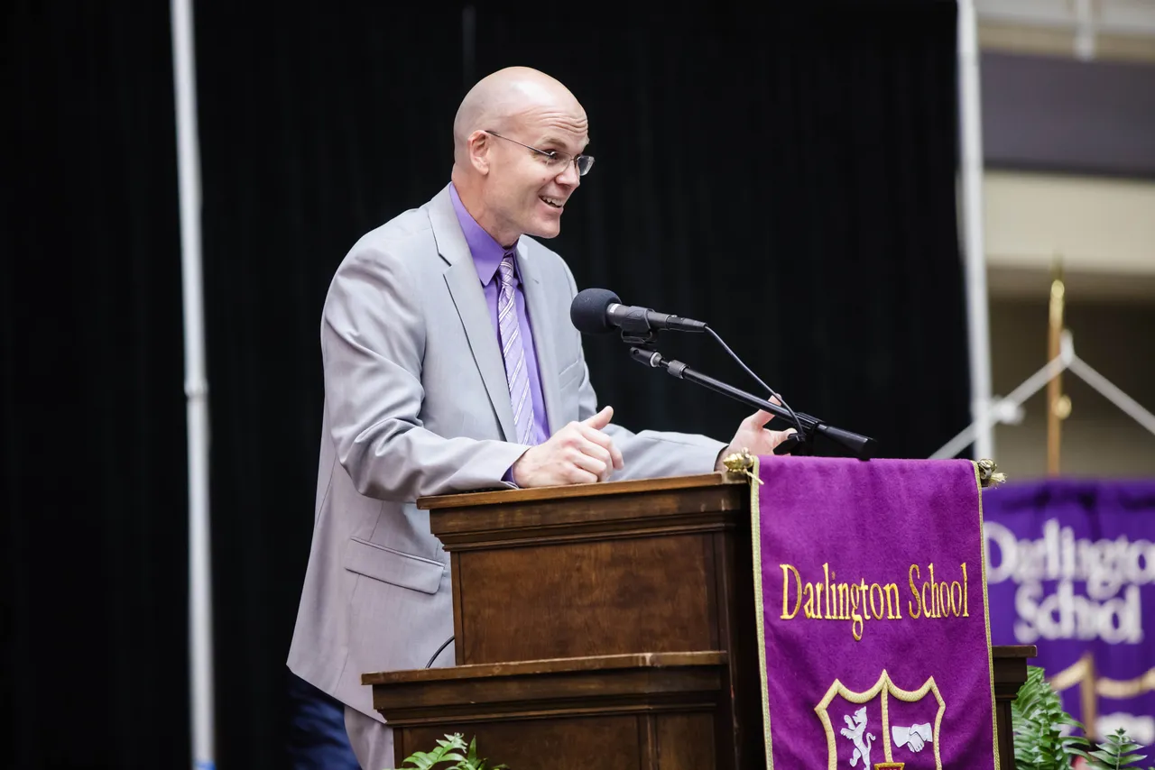 Male teacher and alumnus speaks at a podium during a Darlington School event.