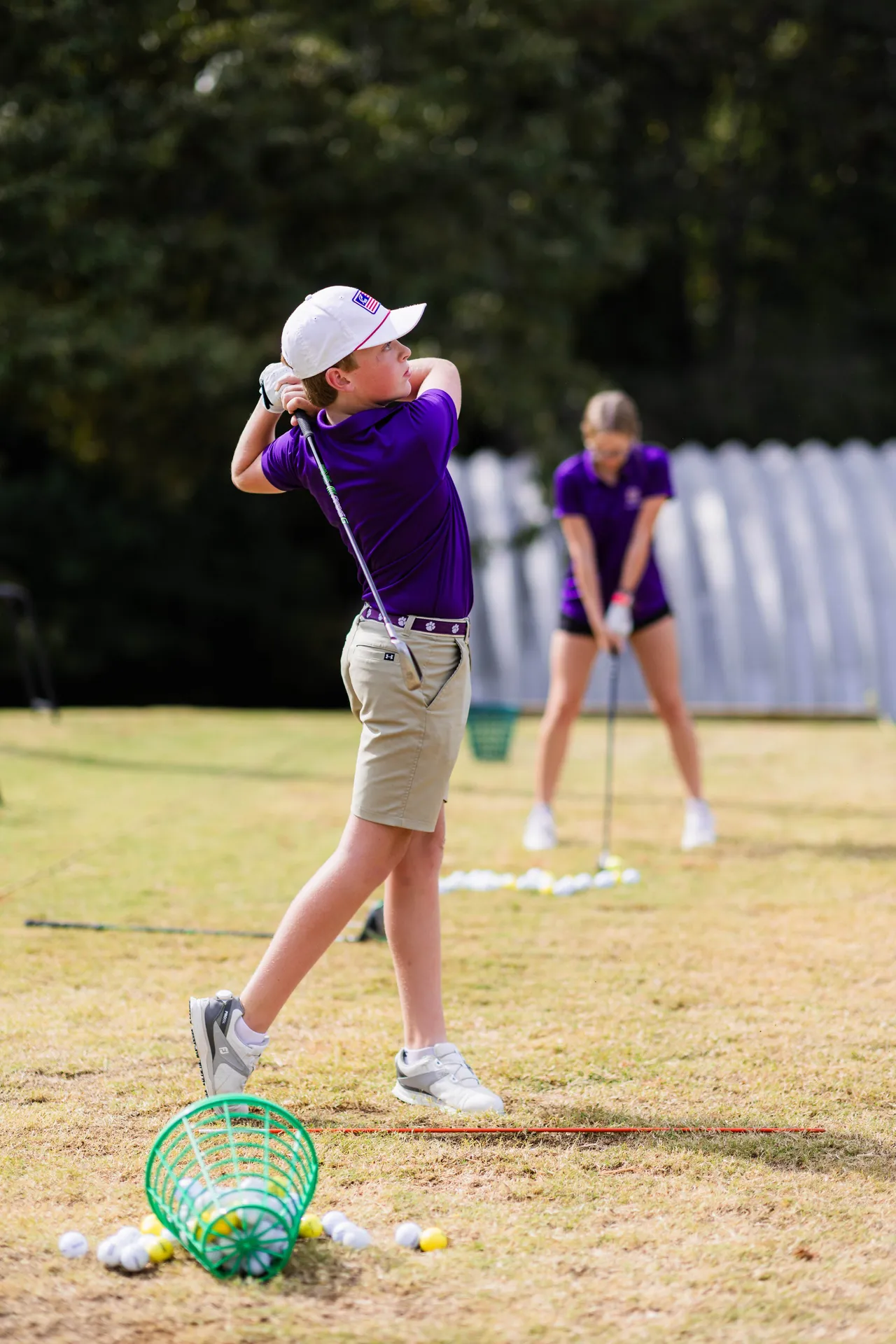 A male middle school golfer practices his swing while hitting a golf ball.