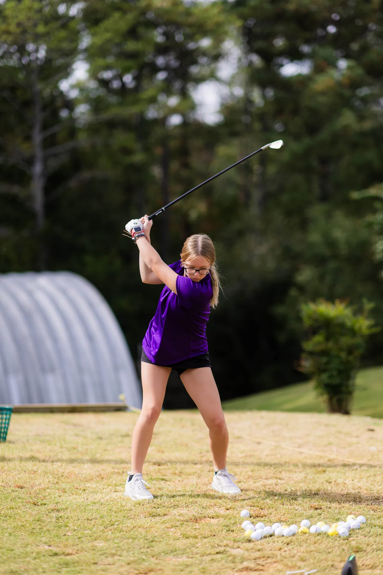 Female middle school golfer practices her swing while hitting golf balls.