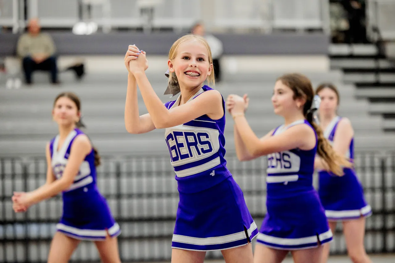Female middle school basketball cheerleaders perform a halftime routine during a basketball game.