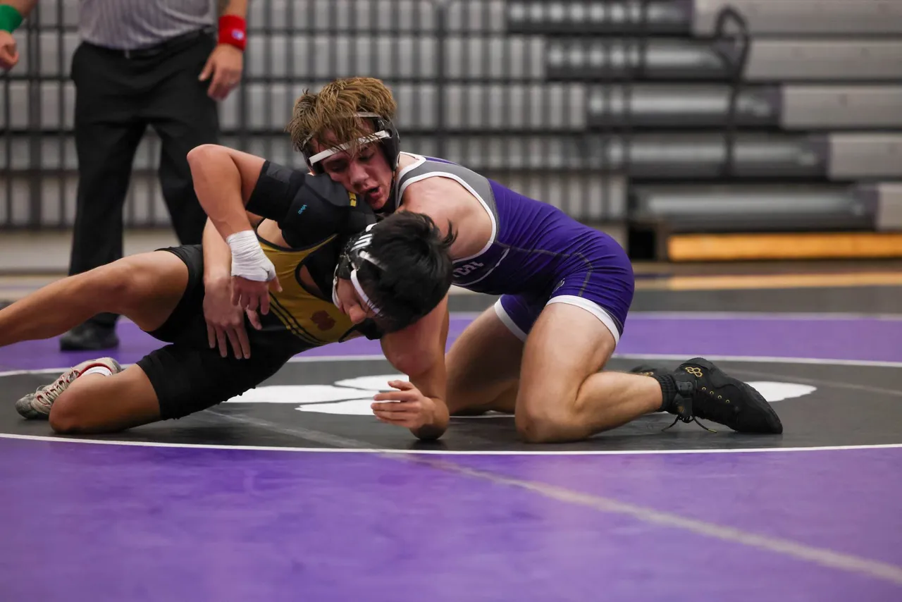 A male middle school wrestler pins an opponent on the wrestling mat during a match.