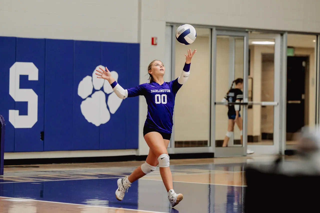 Female middle school volleyball player serves the ball during a game.