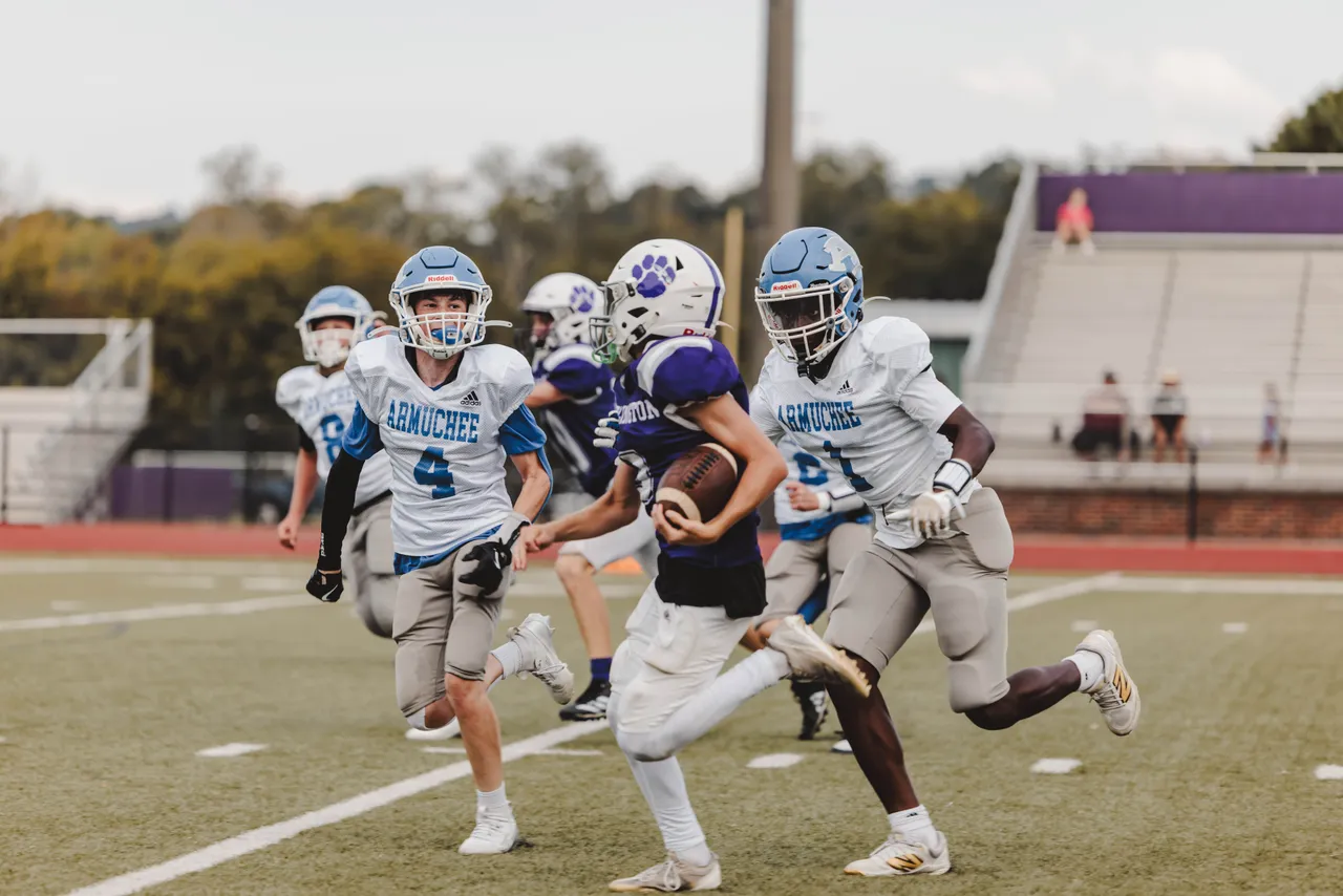 A male middle school football player runs with the ball while opposing players chase him during a game.