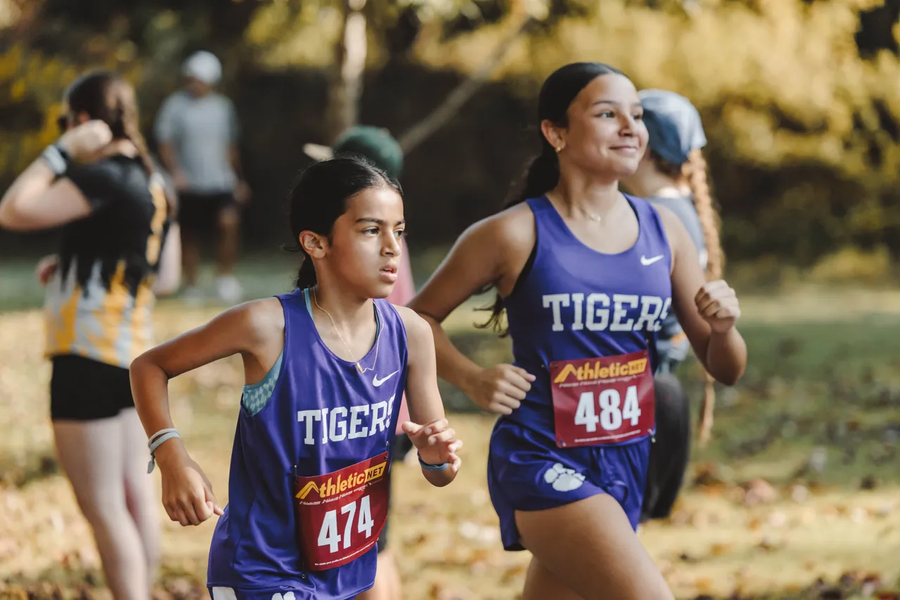 Female middle school cross country runners compete during a race on a cross country course.