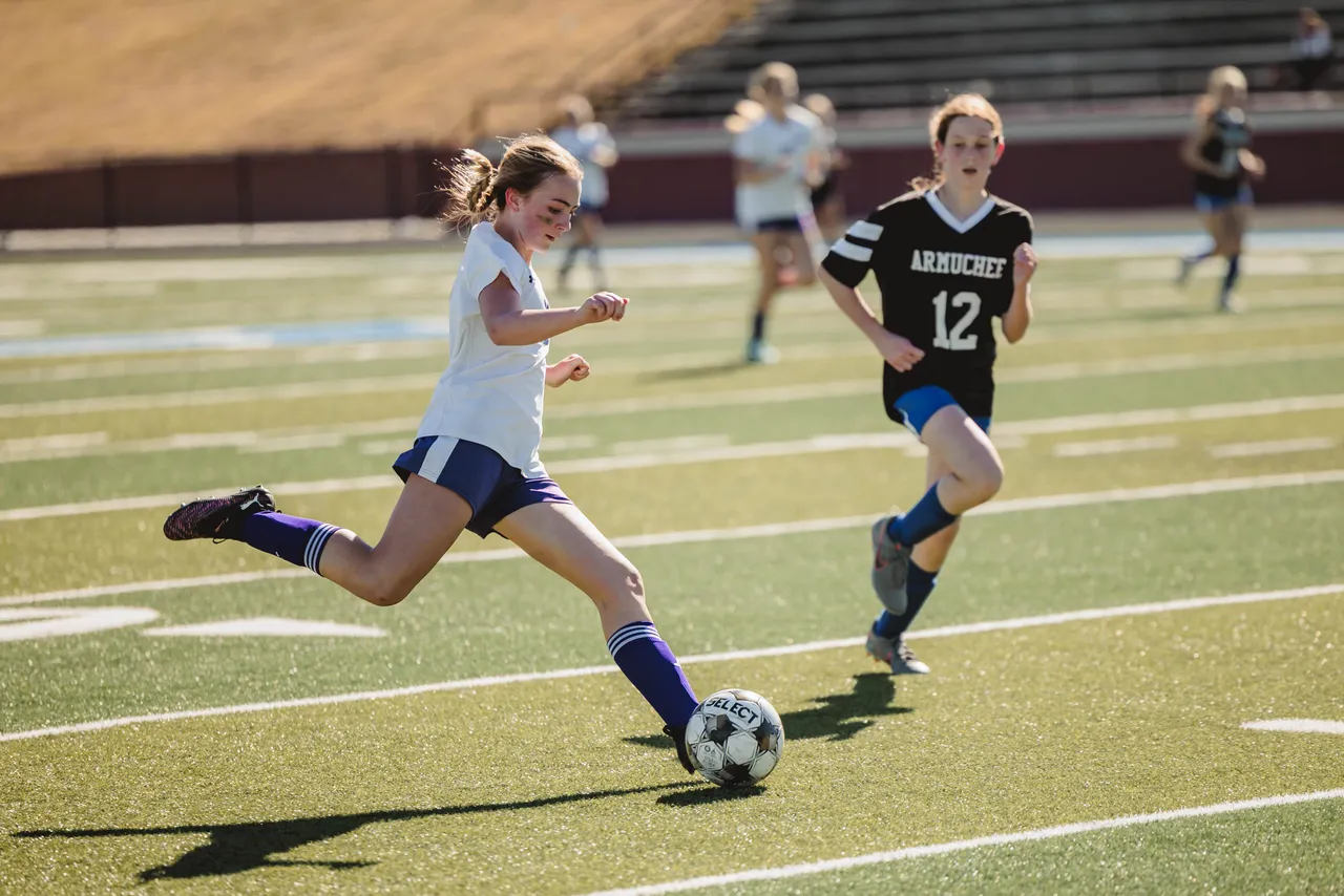 Female middle school soccer player dribbles the ball down the field with an opposing player running alongside her during a game.