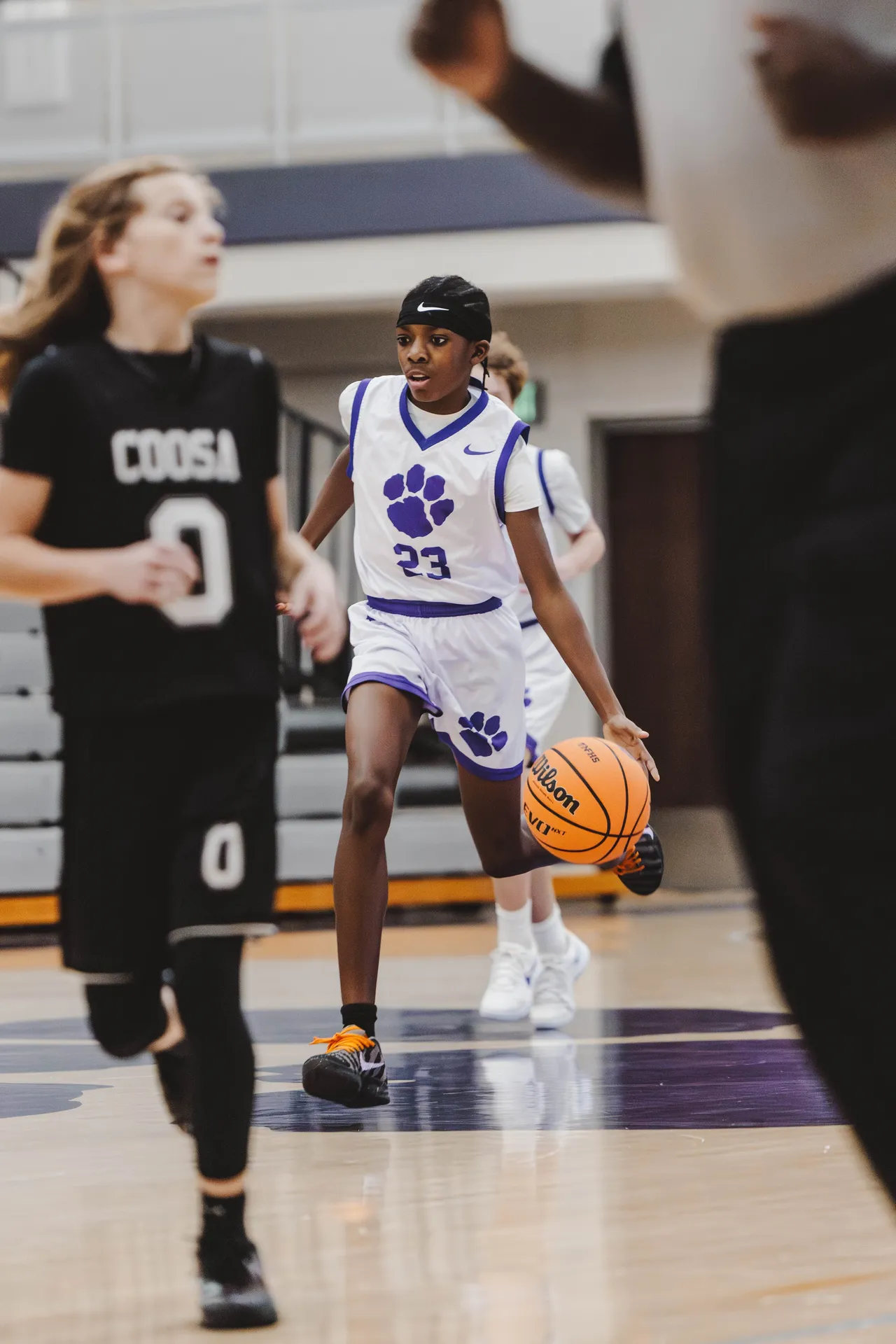 A male middle school JV basketball player dribbles the ball while moving down the court during a game.
