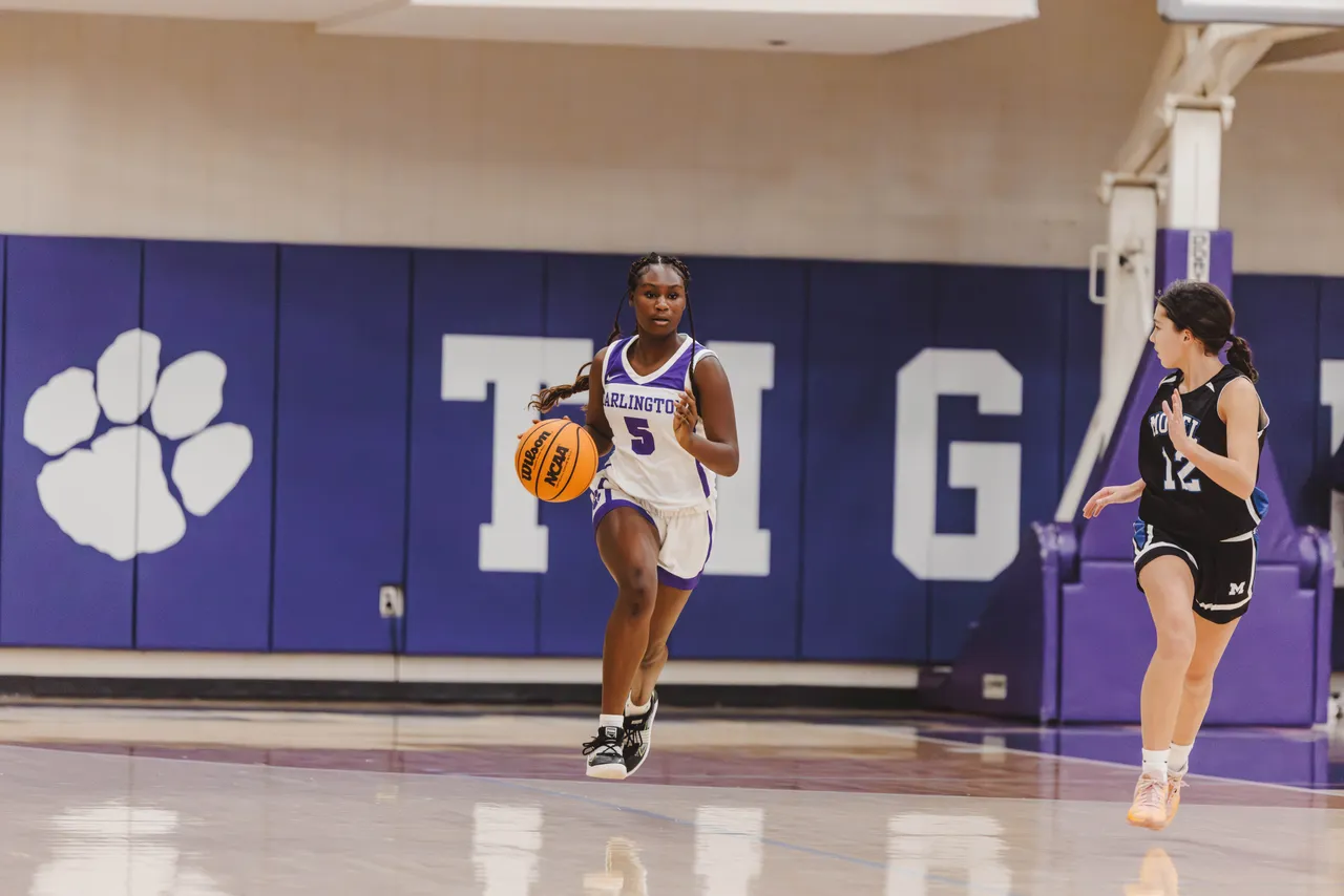 Female middle school basketball player dribbles the ball while moving down the court during a game.