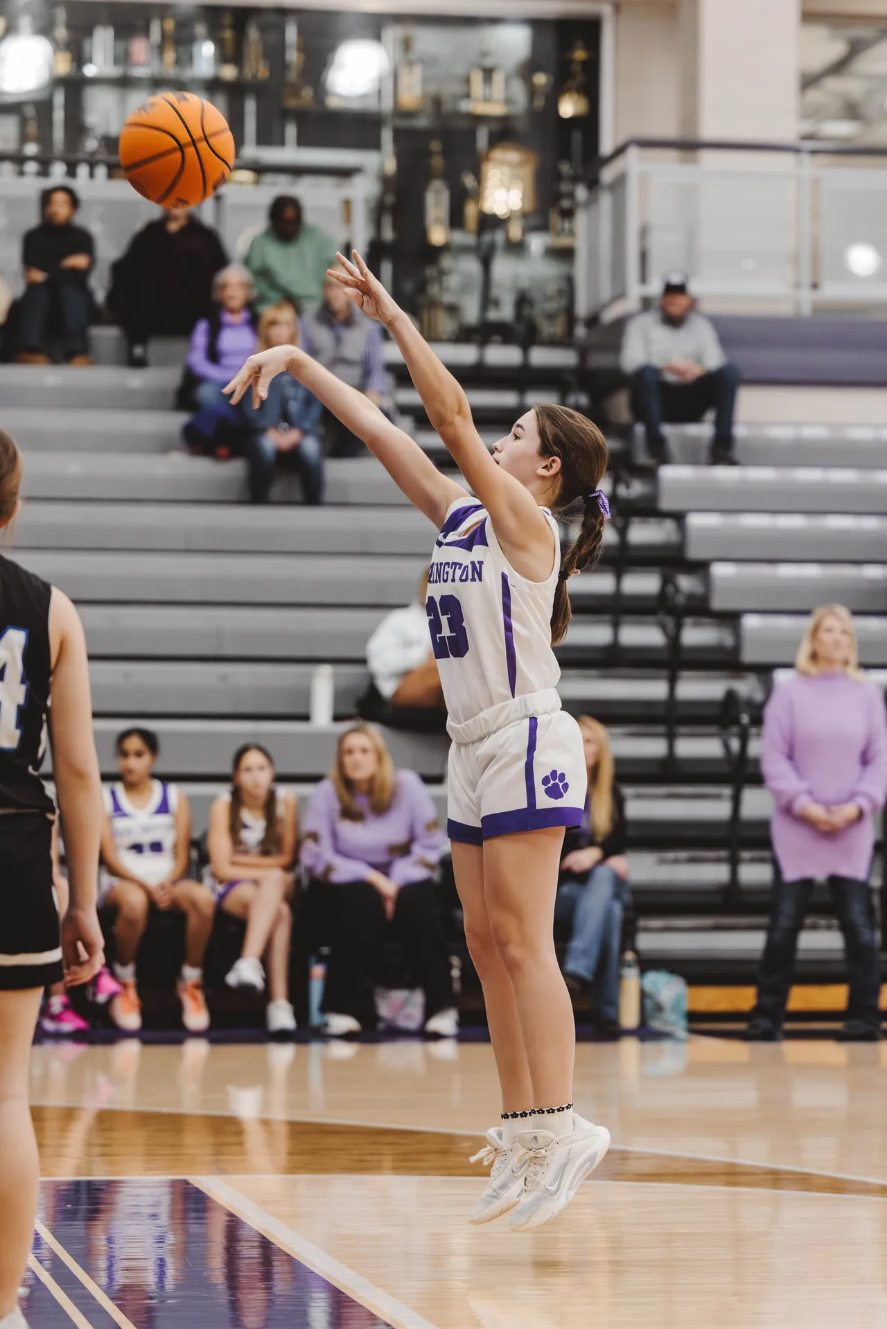 Female middle school JV basketball player jumps and shoots the ball toward the basket during a game.