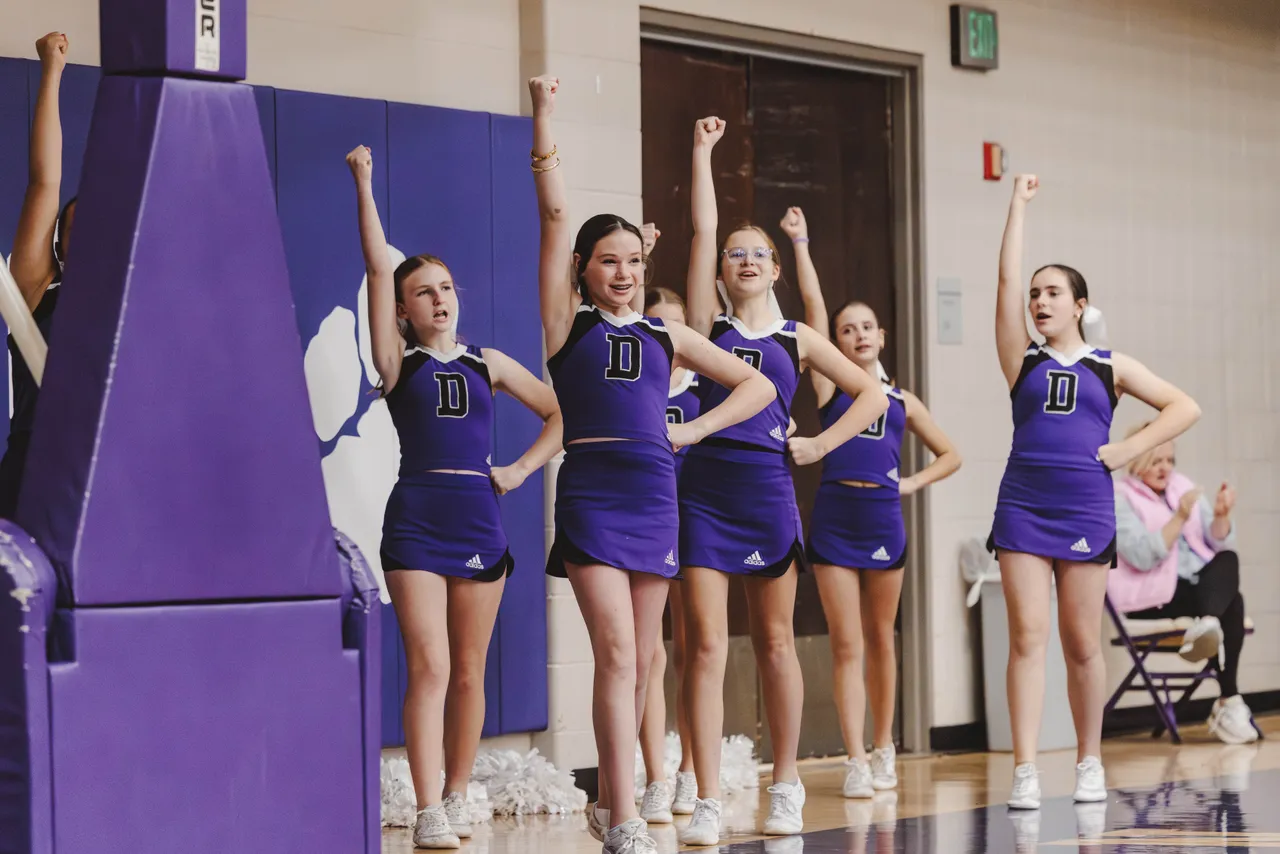Female middle school basketball cheerleaders cheer on the sidelines during a basketball game.