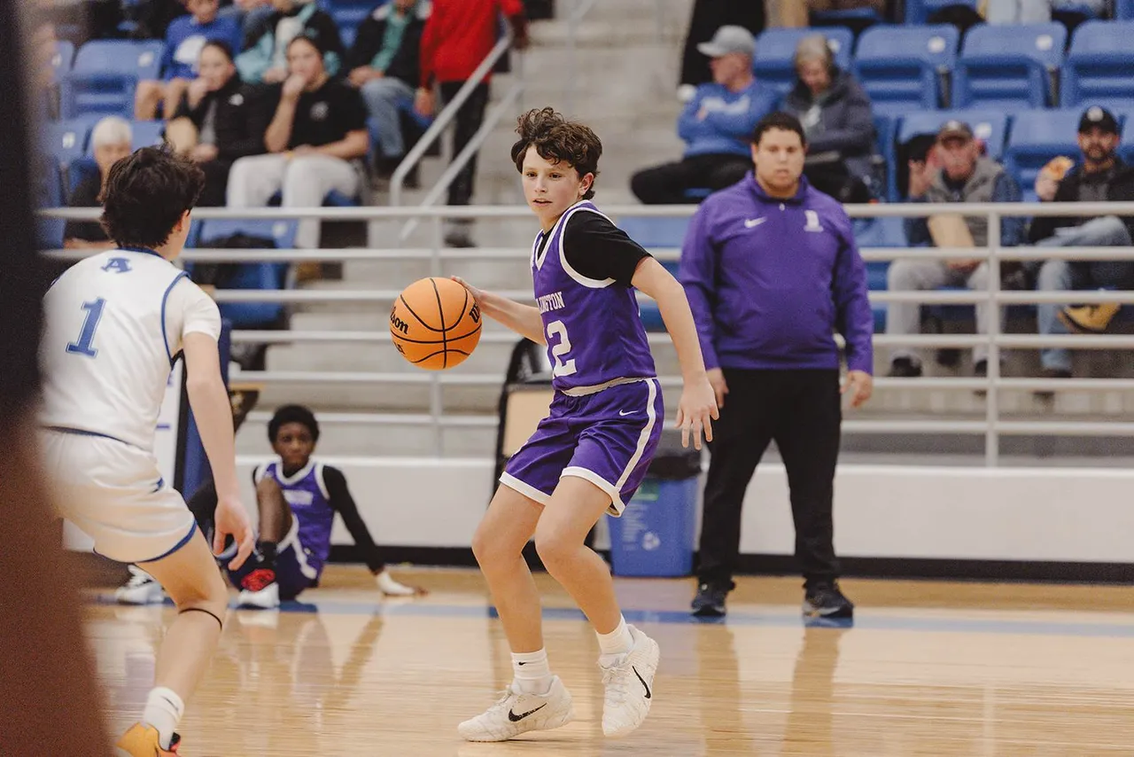 A male middle school basketball player dribbles the ball while moving down the court during a game.