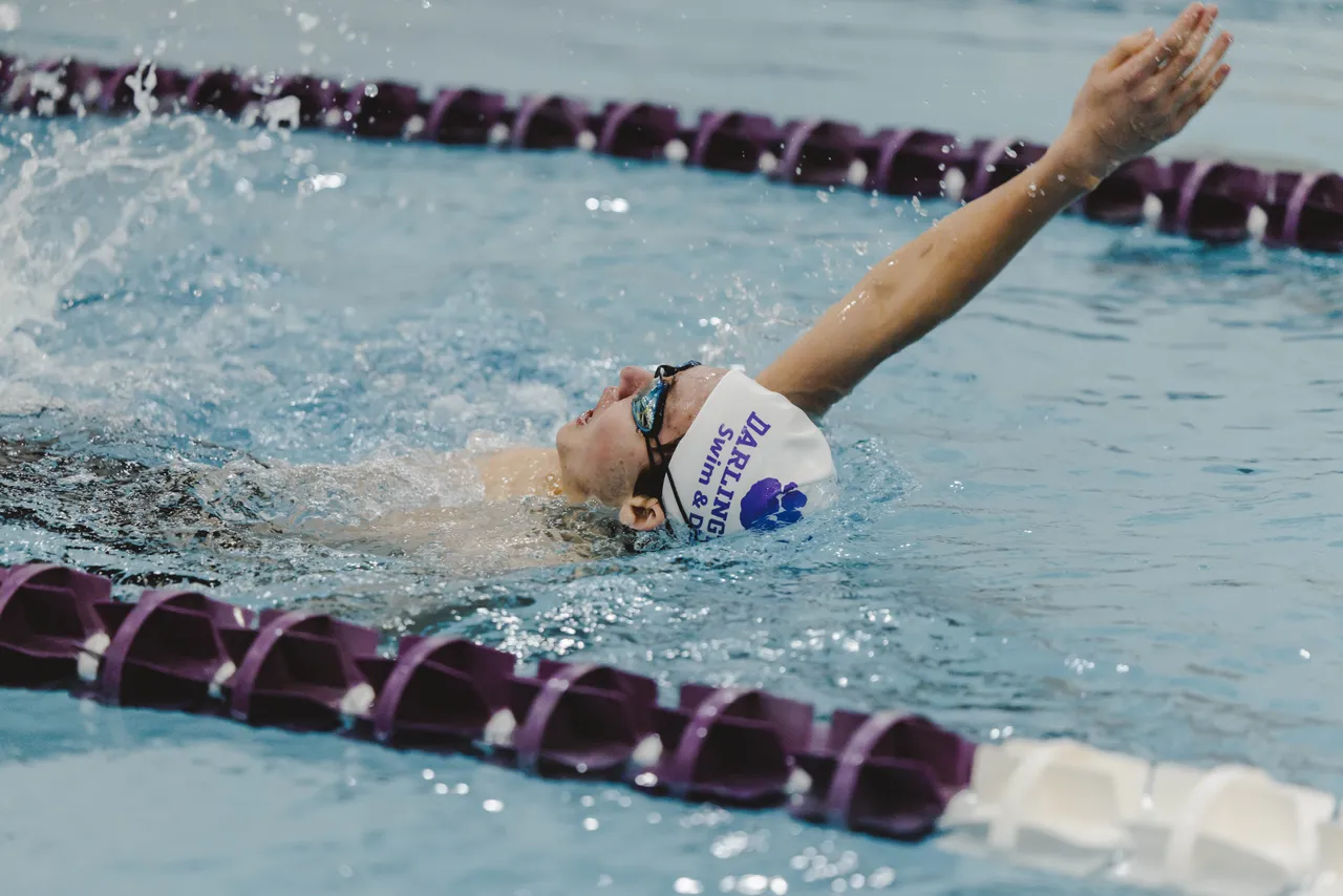 A male middle school swimmer swims backstroke during a swim meet.