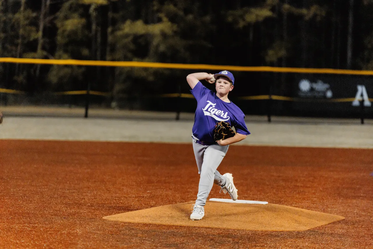 A male middle school JV baseball player throws a pitch from the pitcher’s mound during a game.