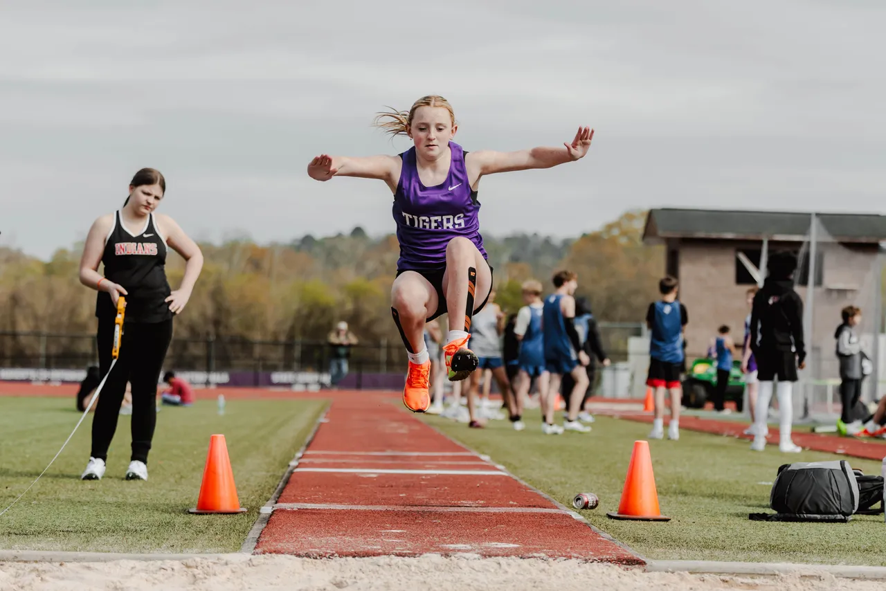 Female middle school track and field athlete jumps into the air during the long jump event.