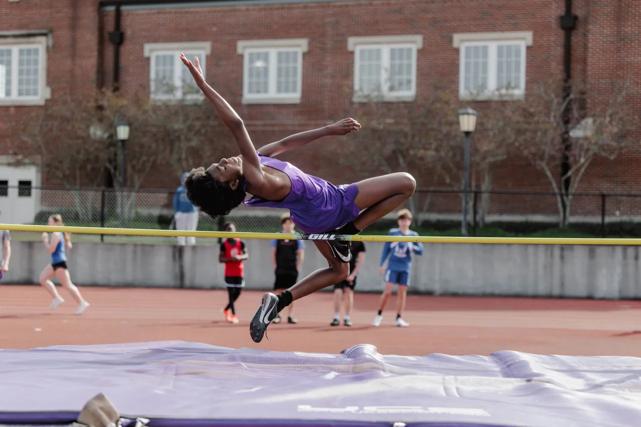 A male middle school student clears the bar during a high jump event at a track and field meet.