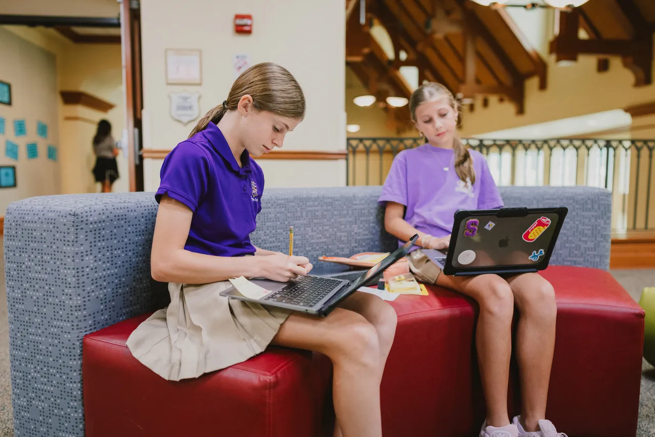 Two female middle grades students work on their MacBook computers
