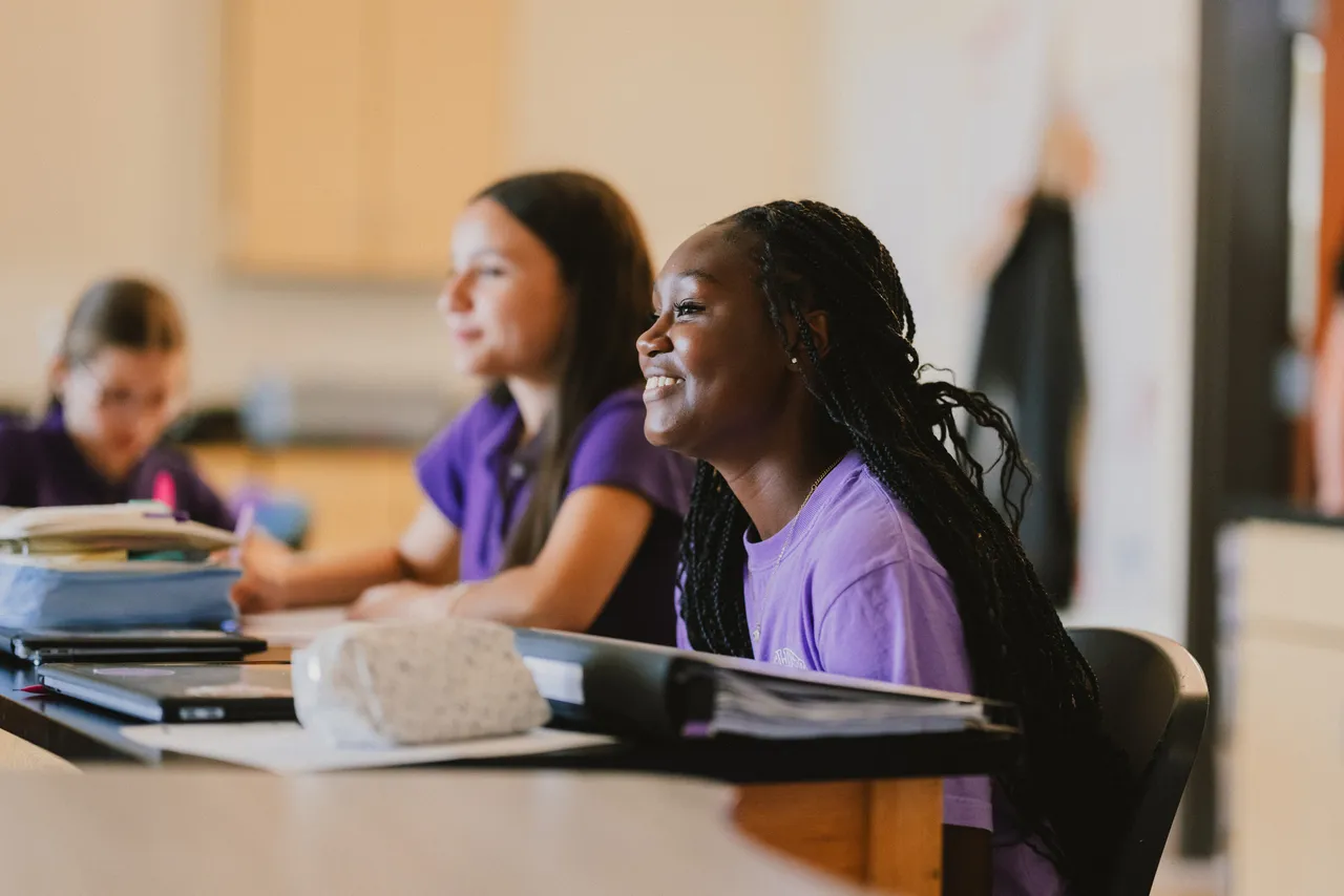 Female middle grades students smile in science class as they listen to their teacher