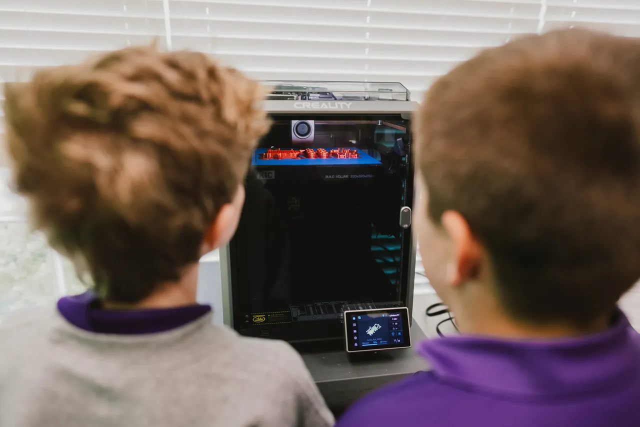 Two male students watch as something is printed in the 3D printer in the makerspace