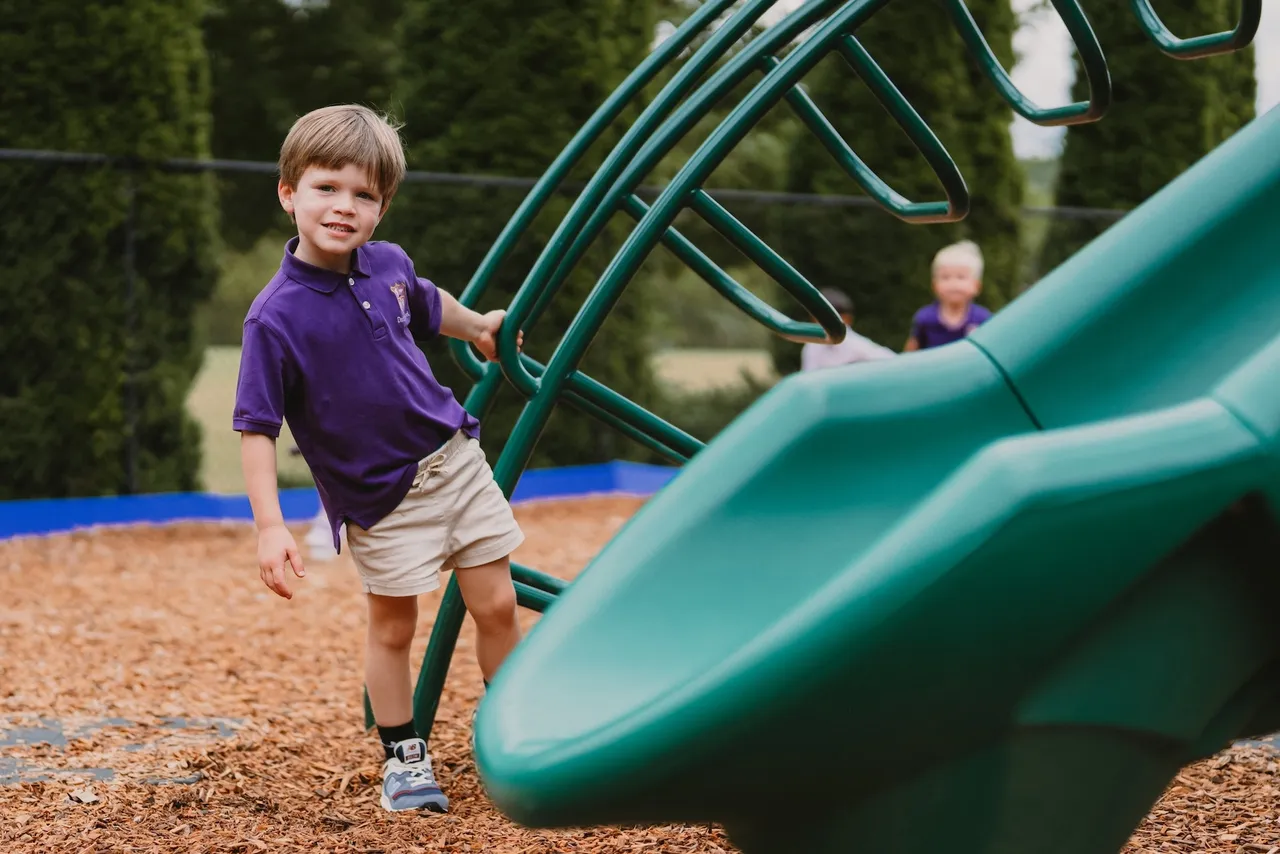Male primary grades student poses at the bottom of the slide on the playground during recess