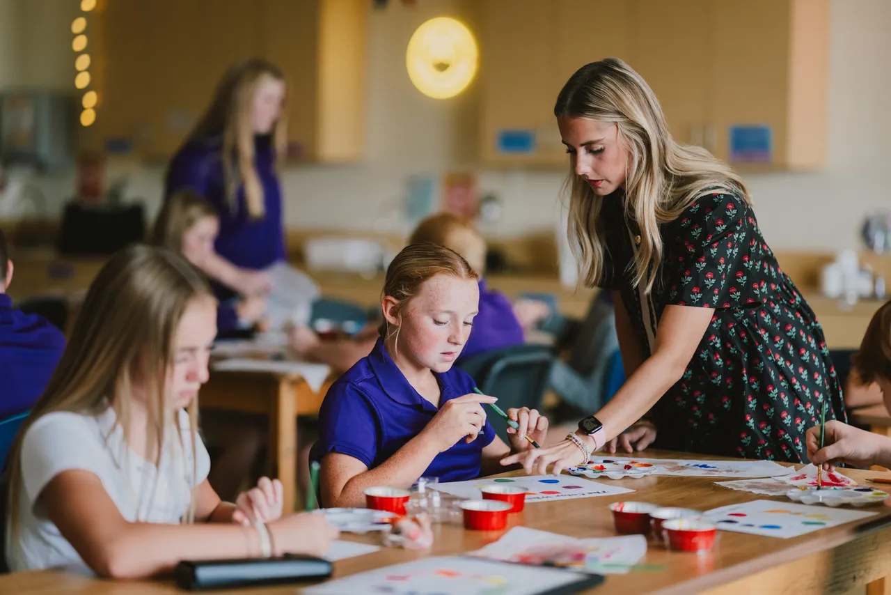 A female art teacher works with middle school girls on a painting activity during art class