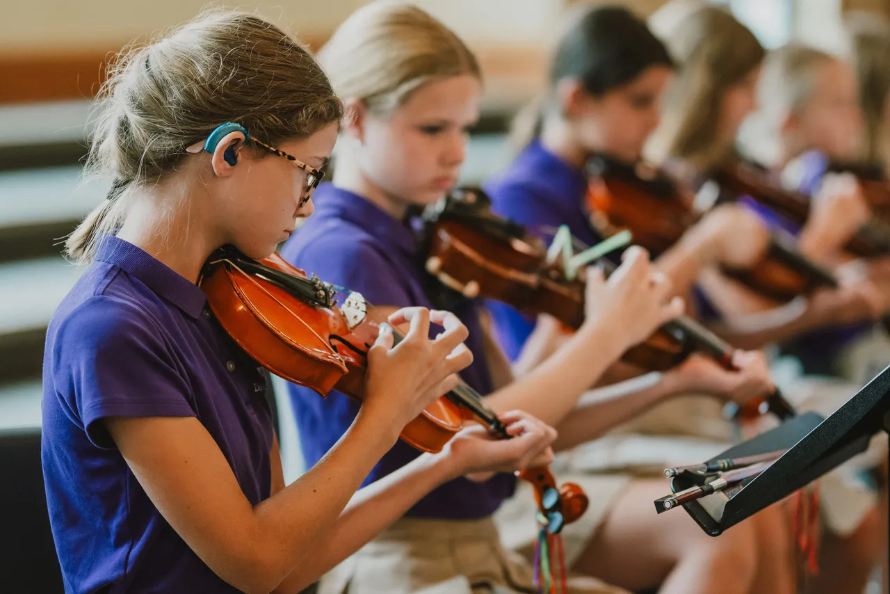 Four middle school students play the violin during their strings class
