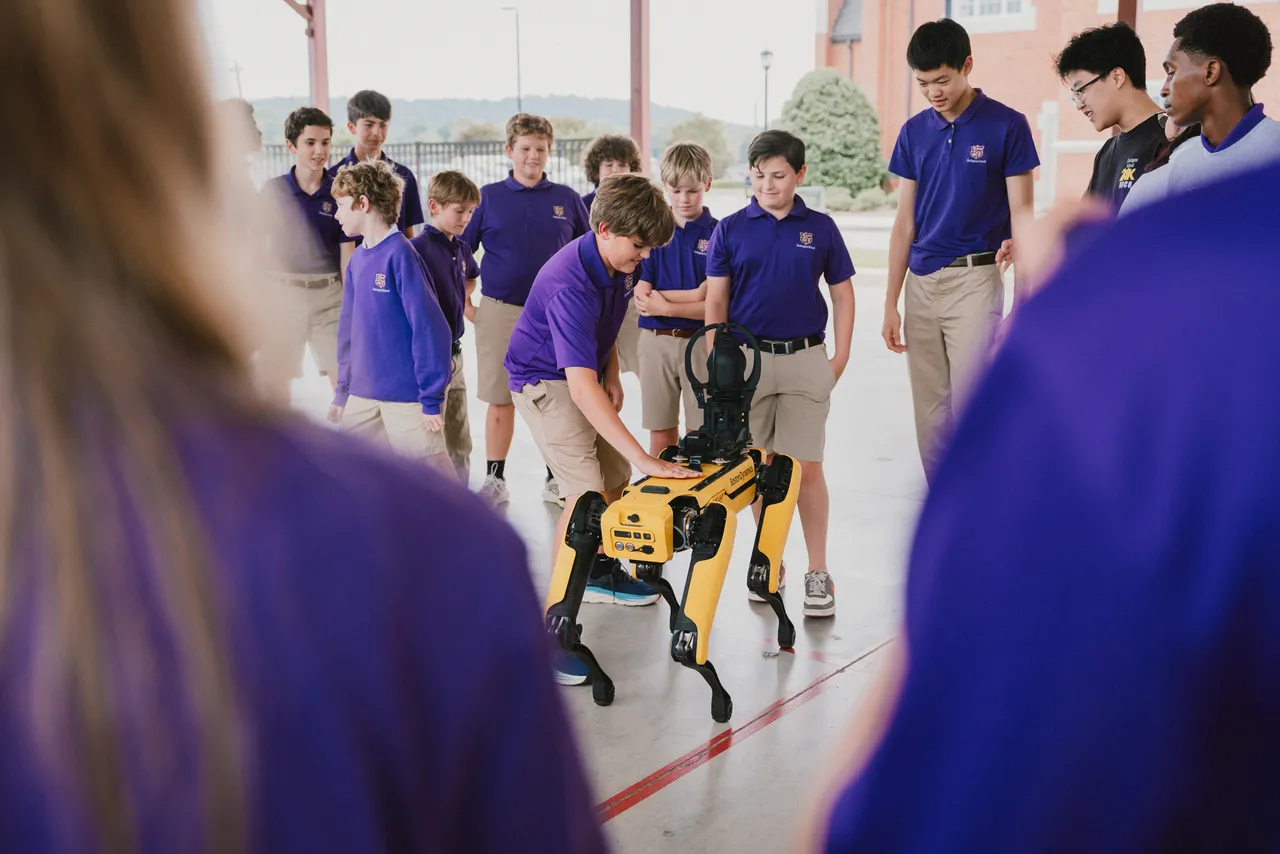 Middle school students gather in the pavilion on campus to observe a robotics demonstration