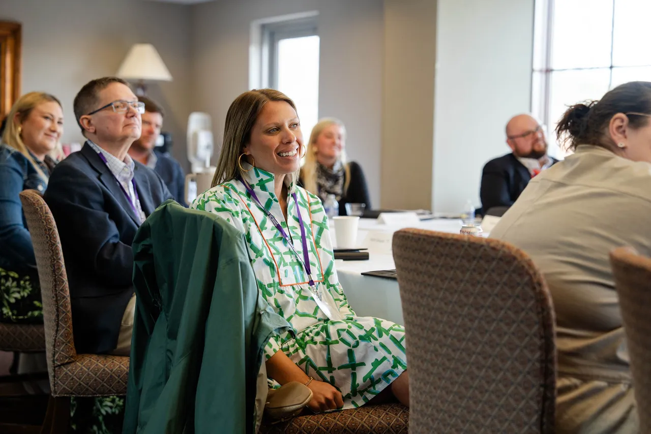 Female alumna sits around a table with other alumni during a discussion.
