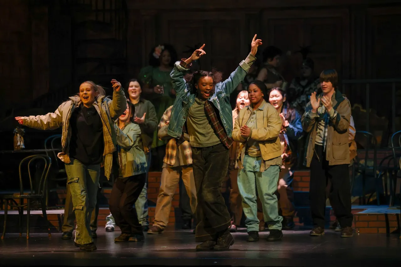 High school students perform on stage, singing and dancing in a theater production