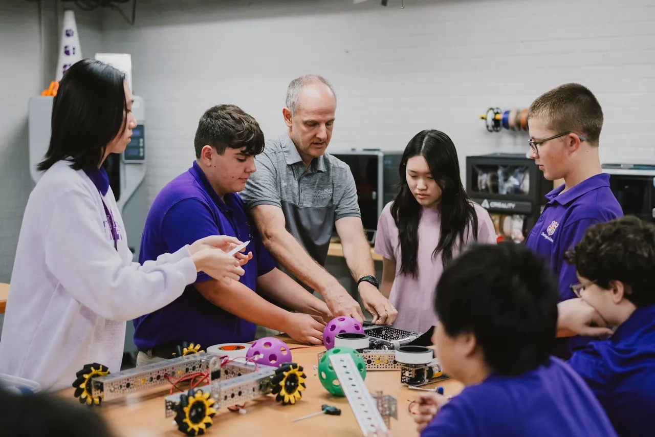 A male teacher works with robotics students in the makerspace building a robot