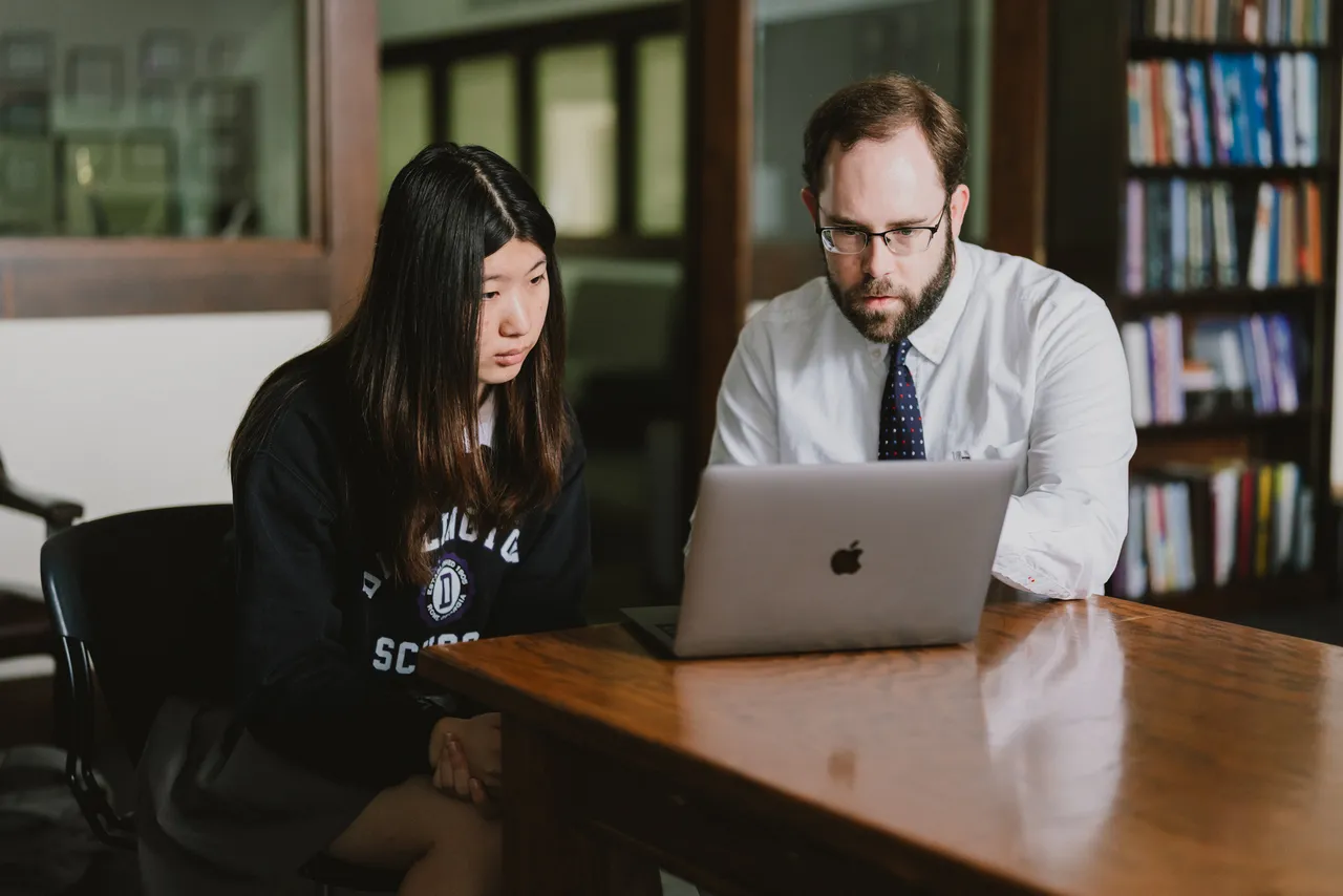 Male teacher works with a female high school student on her laptop in class