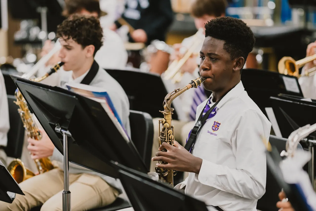 Two male high school students play brass instruments during band class