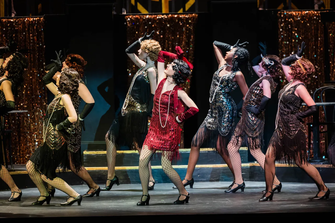 A group of female high school students sing and dance during a theatrical performance of the musical "Chicago"