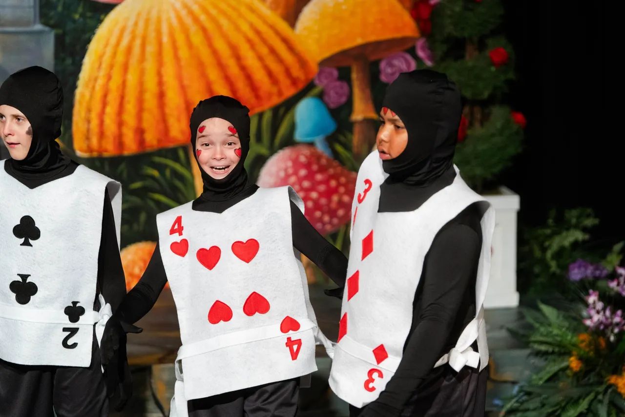 Three male students dressed as playing cards perform on stage in a theatrical production