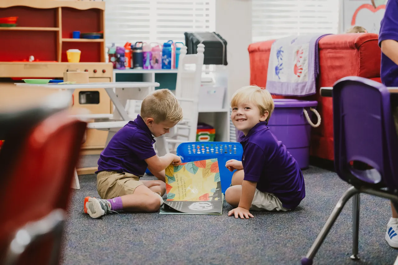 Two male pre-K students read a book together in their classroom