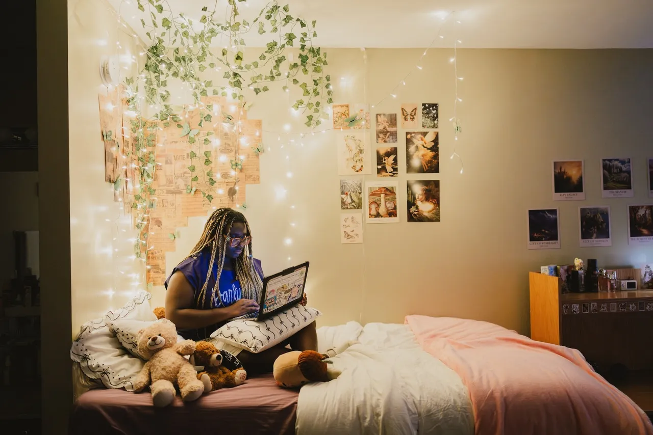 Female boarding student works on her computer in her dorm room which is lit up with fairy lights