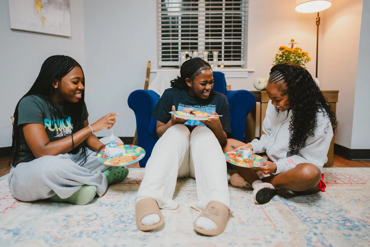 Three female boarding students eat birthday cake in the dorm lounge at a birthday party for a dormmate