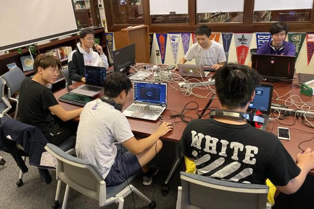 Group of esports students gather around a table with their MacBook computers to play a video game