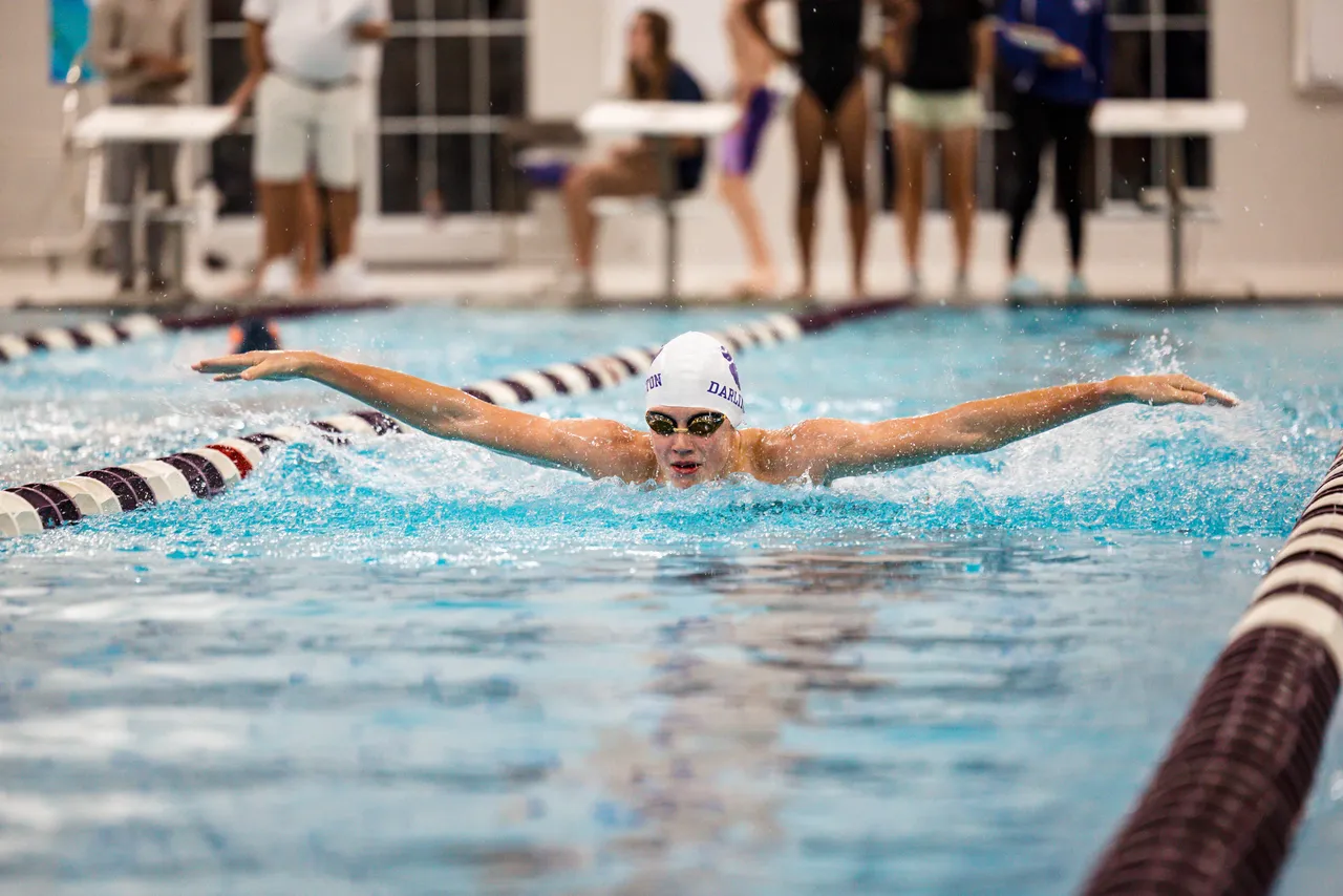Male high school swimmer swims down the lane of the pool during a track meet with his arms stretched out