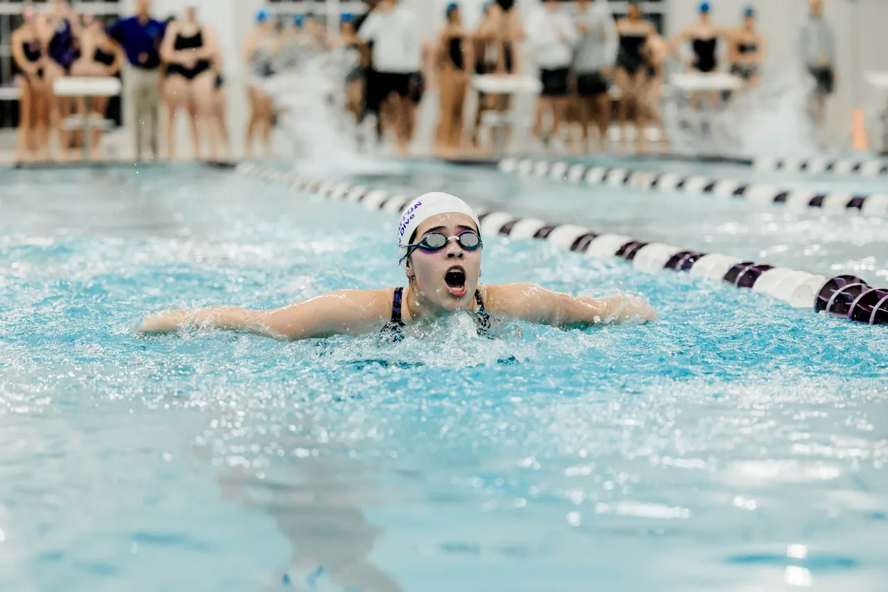 A female high school swim team member swims down her lane during a swim meet in the pool at Darlington School