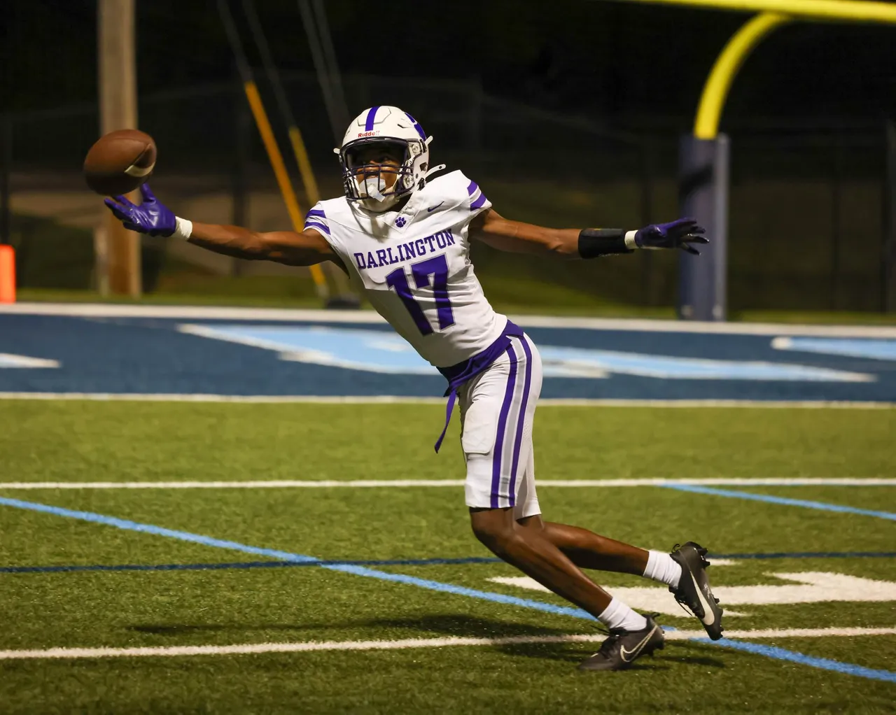 Male high school football player reaches to catch the football near the endzone during a football game