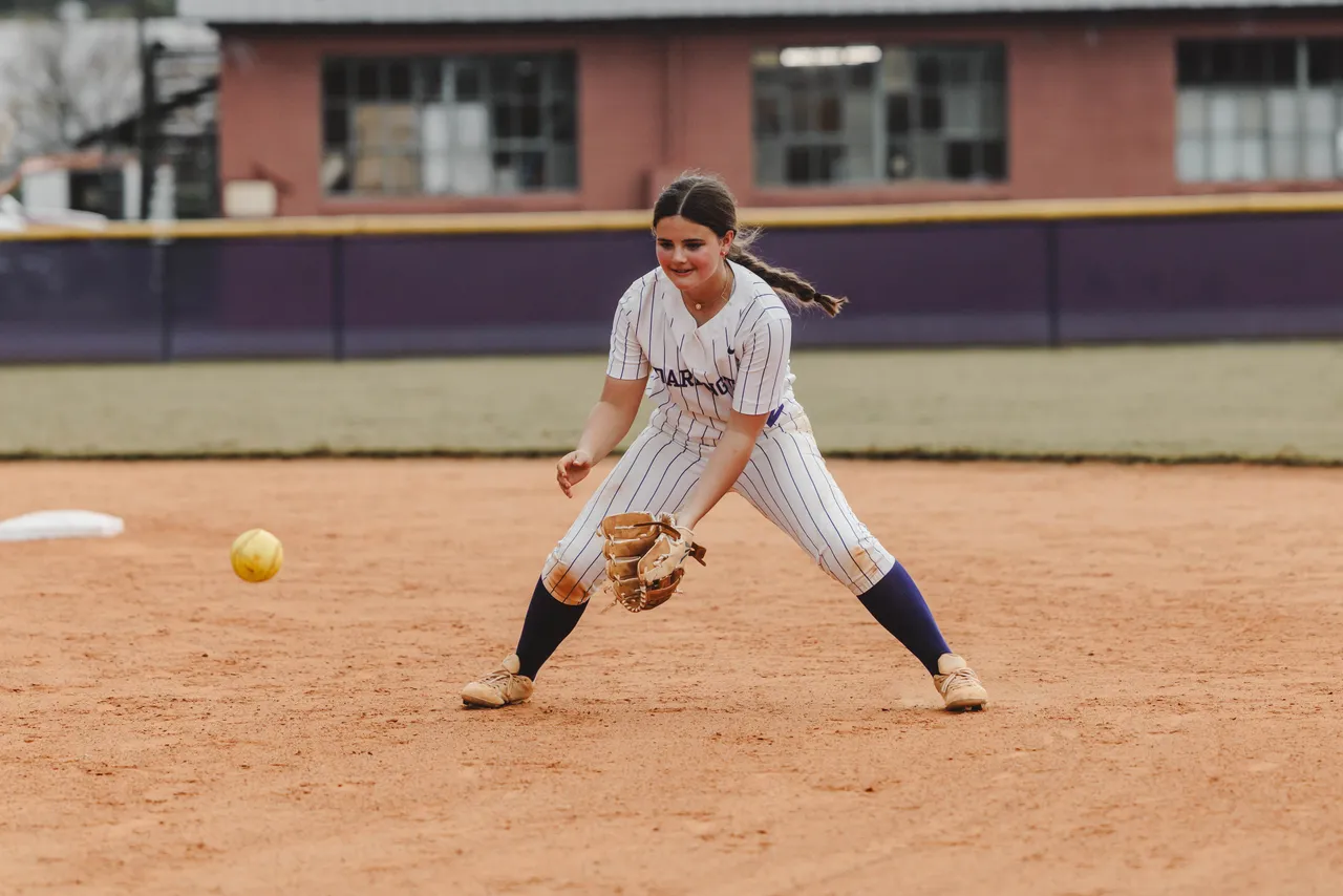 A female high school student gets ready to catch a grounded softball on the softball field