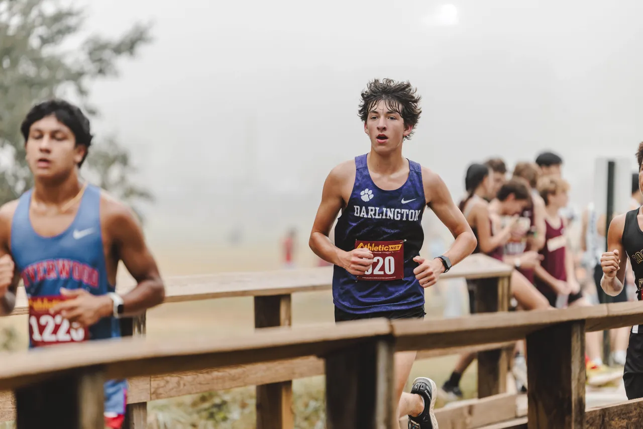 High school boy runs across a bridge on the cross country course during a meet