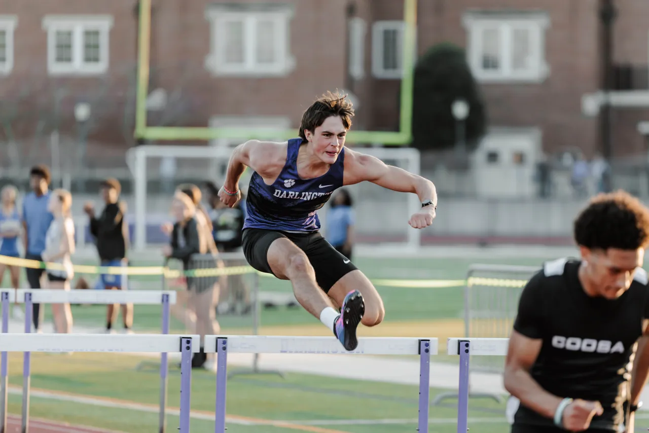 Male high school student jumps hurdles during a track meet
