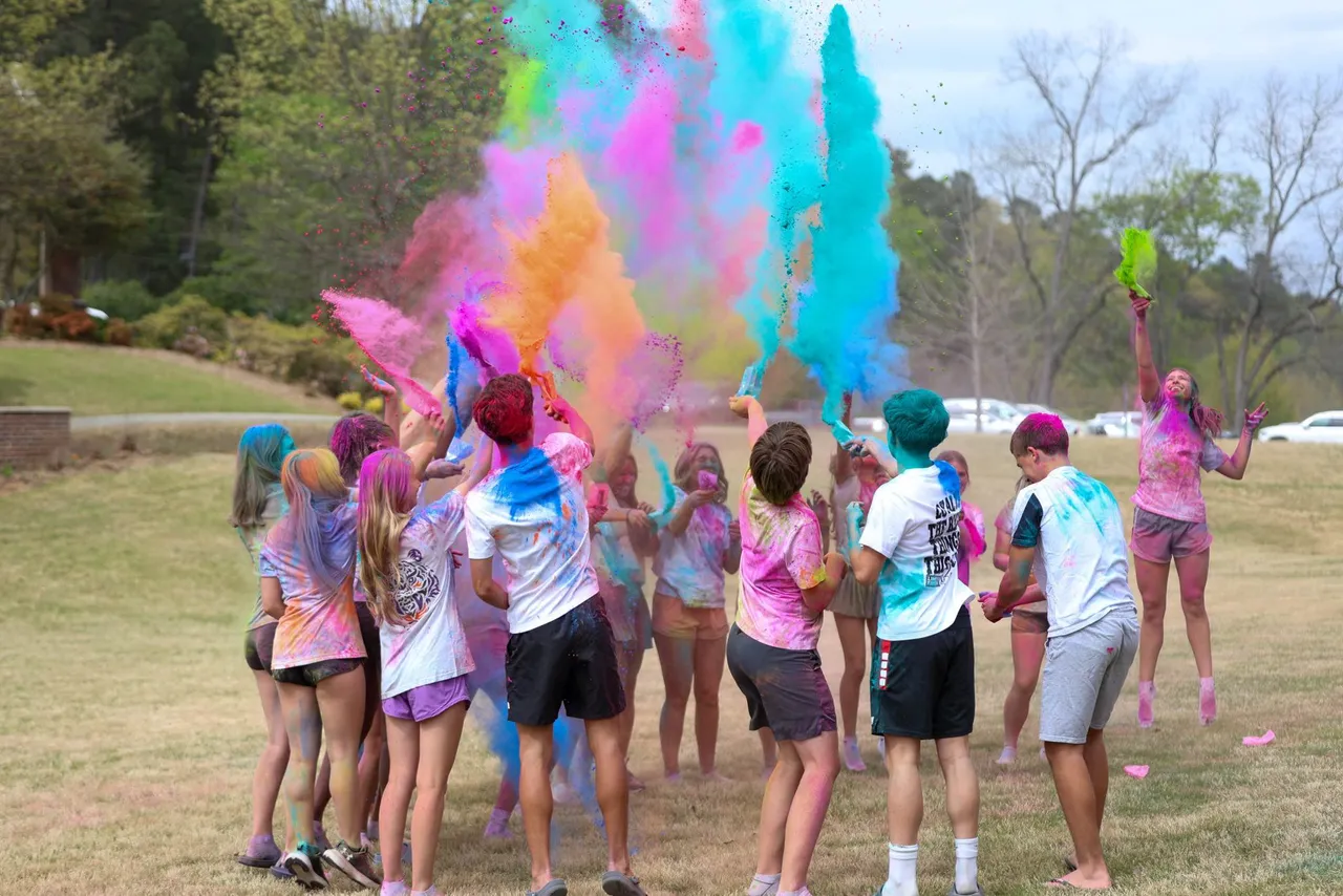 Students celebrate Holi outdoors, tossing colorful powder into the air during a campus celebration.