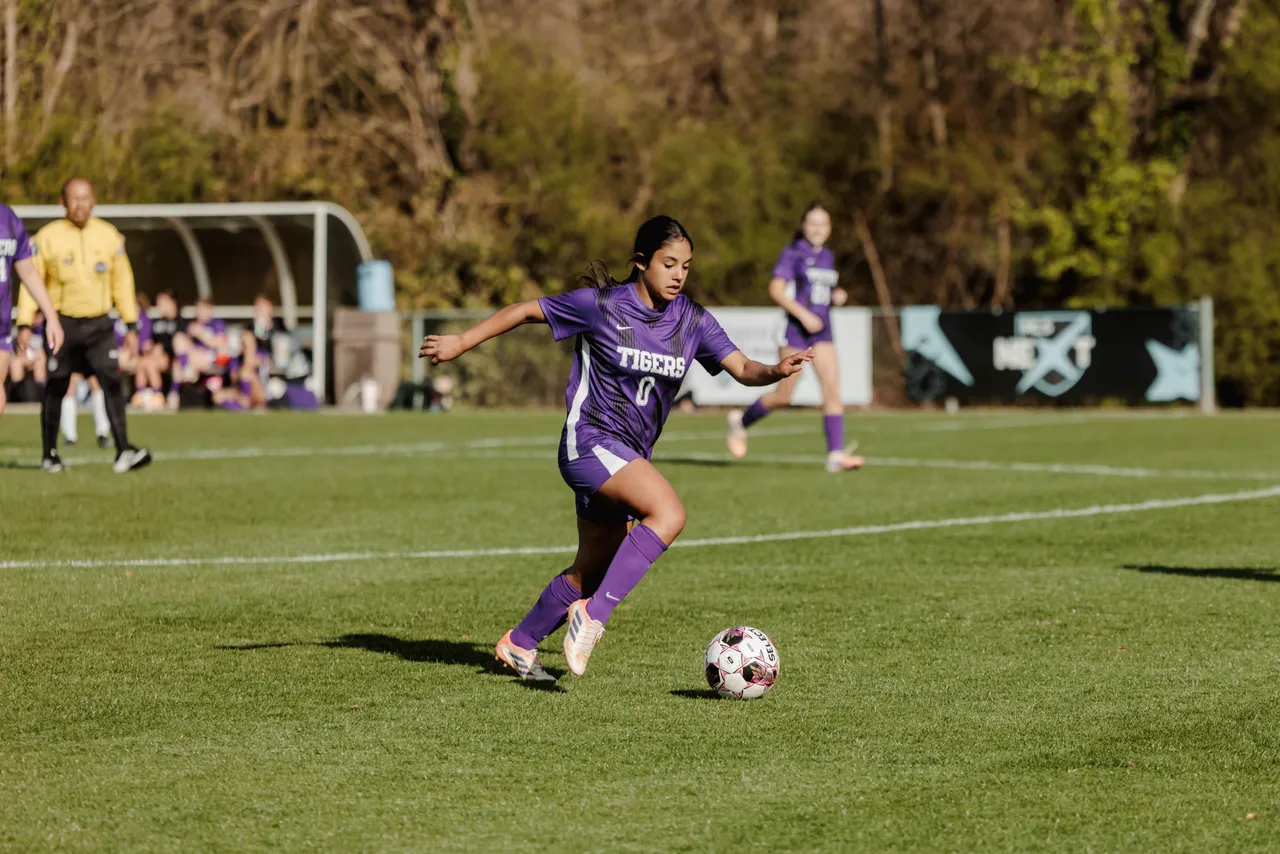 A female high school soccer player prepares to kick the ball down the soccer field